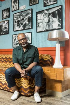 a man sitting on top of a couch in front of a wall covered with pictures