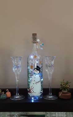 three wine glasses sitting on top of a table next to a bottle with a snowman painted on it