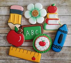 several decorated cookies are on a table with a ruler, apple, pencil and flower