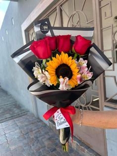 a woman holding a bouquet of flowers in front of a building with red roses and sunflowers