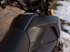 the back end of a motorcycle parked in front of a stone wall and snow covered ground