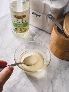 a person is spooning liquid from a glass bowl on a marble counter top next to a blender