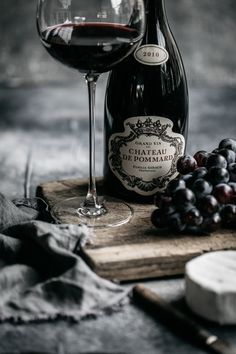 a bottle of wine and some grapes on a wooden board next to a glass of red wine