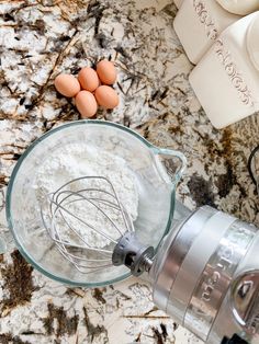 eggs and flour in a glass bowl next to a blender on a marble counter