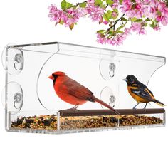 two birds sitting on top of a bird feeder with pink flowers in the back ground