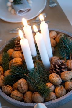 three candles are lit in a bowl filled with nuts and pineconis on a table