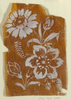 a piece of paper with flowers and leaves painted on it, sitting on top of a table