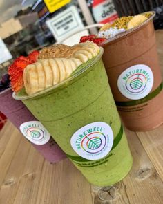 three smoothies with banana slices and strawberries in them sitting on a wooden table