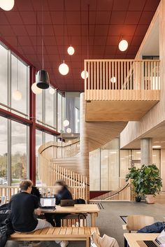 two people sitting on benches in an open area with large windows and wooden staircases