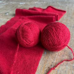 two balls of red yarn sitting on top of a wooden table next to a red cloth