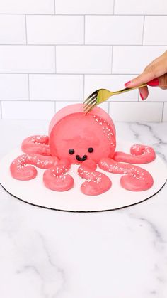 someone is decorating a cake with pink icing and an octopus on it's face