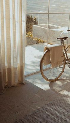 a bike parked next to a window with curtains on it's sides and the sun shining through