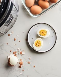 two hard boiled eggs on a plate next to an open instant pot with broken eggs in it