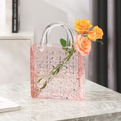 a pink bag with flowers in it sitting on a marble table next to a book