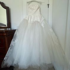 a white wedding dress hanging on a wall in front of a dresser with a mirror