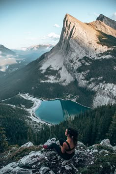 a woman sitting on top of a mountain next to a lake