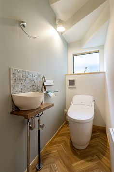 a white toilet sitting next to a bathroom sink under a window on top of a wooden floor