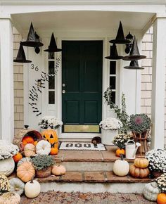 pumpkins and gourds are on the front steps of a house with black lanterns