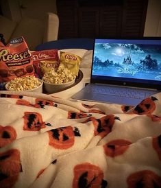 an open laptop computer sitting on top of a bed next to a bowl of popcorn