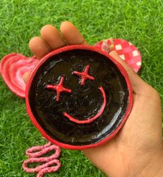 a hand holding a small red and black object with a smiley face painted on it