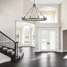 an empty foyer with white walls and wood floors, chandelier over the door