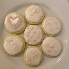 six decorated cookies on a white plate with pink bows and heart shaped frosted sugars