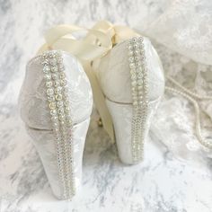 two white shoes with bows and pearls on them sitting on a marble surface next to lace