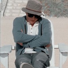 a man sitting on top of a white bench wearing a hat and sunglasses with his arms crossed