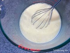 a glass bowl filled with white liquid and whisk