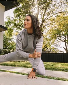 a woman is doing yoga outside on the sidewalk in front of a house with trees