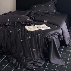 a bed with black sheets and pillows on top of it next to a night stand