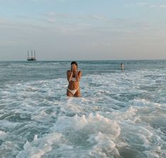 a woman is standing in the ocean with her hand up to her face