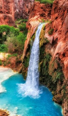 a waterfall in the middle of a canyon with blue water flowing from it's sides