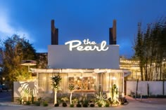 the front of a restaurant at night with lights on it's windows and palm trees