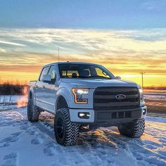 a white truck parked on top of snow covered ground in front of a sun set