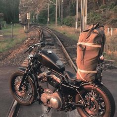 a motorcycle parked on the side of train tracks with a bag strapped to it's back