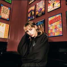 a woman leaning against a wall covered in posters