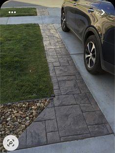 a car parked on the side of a road next to a grass covered field and sidewalk