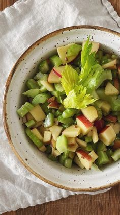 a white bowl filled with green and red fruit on top of a wooden table next to a napkin