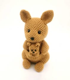 a crocheted teddy bear sitting next to a smaller stuffed animal on a white background