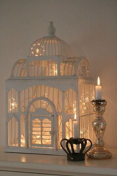 a white birdcage with lights on it and a candle in front of it