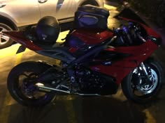 a red and black motorcycle parked next to a white car in a parking lot at night