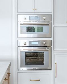 an oven built into the side of a white cabinet in a kitchen with gold handles