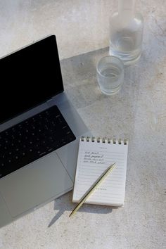 an open laptop computer sitting on top of a table next to a notepad and pen