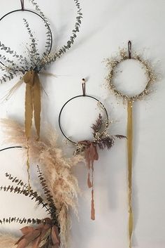 three circular wall hangings decorated with dried plants and feathers, one is white the other is gold