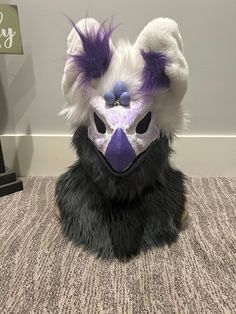 a stuffed animal wearing a purple and white mask on top of a carpeted floor