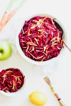 a bowl filled with red cabbage next to an apple