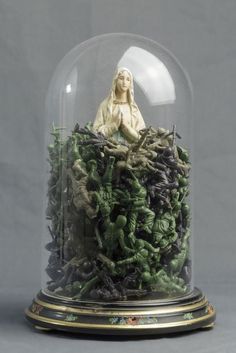 a glass clochet with a statue in it on top of green plants under a dome