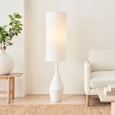 a white table lamp sitting on top of a wooden floor next to a couch and coffee table