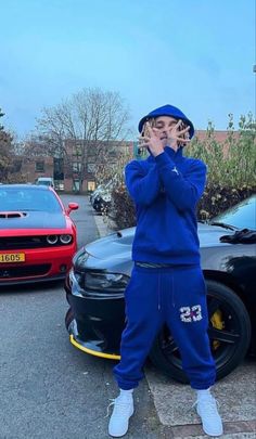 a person standing in front of a car talking on a cell phone while wearing a blue hoodie and sweatpants